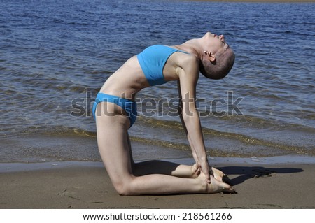 Bald woman in yoga position ustrasana, or camel, on a beach.