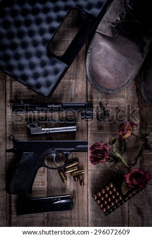 Still Life Disassembled handgun ,Bullet ,Boots, Rose on wood floor.Top view , Dark tone picture style