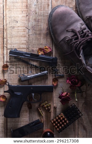 Still Life Disassembled handgun ,Bullet ,Boots, Rose and wood space on wood floor.Top view , Dark tone picture style