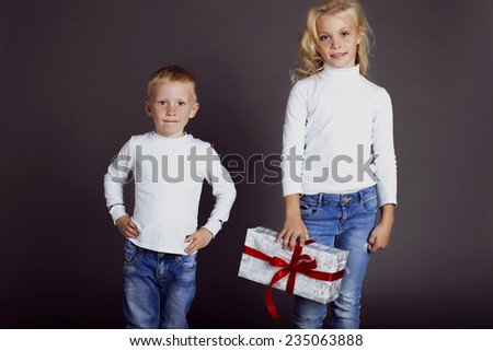 Christmas photo with small children dressed in jeans and a white sweater smiles and holding a box with a gift
