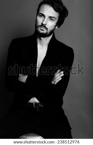 Fashion studio photo of sexy brunette handsome man dressed in a black jacket and jean whith belt sitting on the cheir,bussines