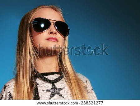 Fashion photo of cute little blond girl with long straight hair wearing in  jeans, sweater with stars print and sunglasses posing in the studio