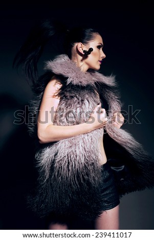 fashion photo of sexy brunette woman in fur coat and leather shorts with bright makeup and purple lips posing,moving  in studio
