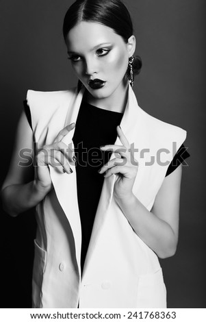 Elegance fashion photo of glamor beautiful brown-haired woman in a black sexy dress with white vest and earrings posing in the studio,luxury