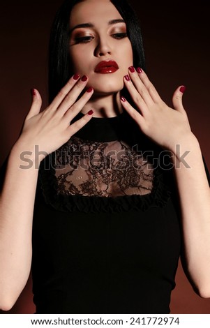 fashion photo of sexy brunette woman in black dress and heeled shoes with red lips and hair posing at studio