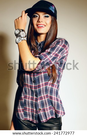 fashion swag style photo of beautiful girl with dark long straight hair in a cap,plaid shirt and watches posing at studio