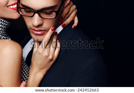 Fashion photo of office romance of sexy lovers,pretty blond woman with watch,red lipstick,and handsome brunette businessman wearing in suit,tie,glasses,they are hugging and kissing on Valentine\'s day
