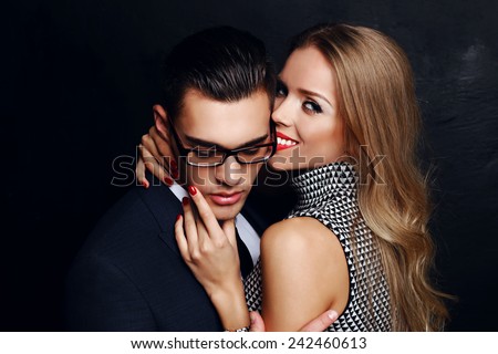office romance of lovers of blond woman with great smile,white teeth,bright makeup and handsome brunette businessman wearing in format suit,tie,glasses, they are hugging and kissing on Valentine\'s day