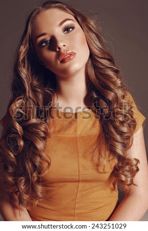 Fashion portrait of young pretty woman with blond curly lush hair and beautiful bright makeup wearing yellow dress, the wing blows her hair