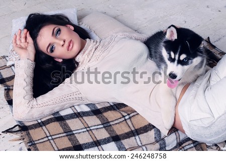 Studio photo of beautiful sexy brunette women with long straight hair wearing in cream sweater relaxing at home, lying on the wood floor and blanket with a cute little dog of Husky