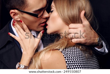 Fashion photo of office romance of sexy lovers,pretty blond woman with watch,red lipstick,and handsome brunette businessman wearing in suit,tie,glasses,they are hugging and kissing on Valentine\'s day