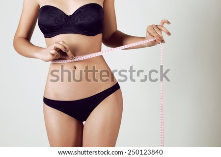 Fashion photo of sexy young woman in lingerie with slim body sitting on a diet and measuring the waist with a centimeter tape