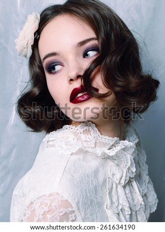 Fashion photo of pretty young curly woman with big blue beautiful eyes wearing a retro style in pink suite earrings ,sitting on a swing and posing at studio