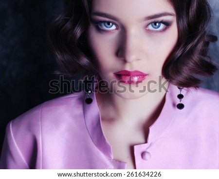 Fashion photo of pretty young curly woman with big blue beautiful eyes wearing a retro style in pink suite earrings ,sitting on a swing and posing at studio