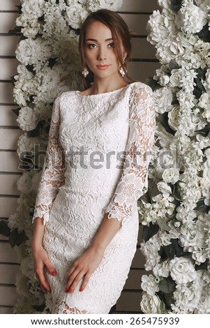 Fashion portrait of sexy woman with brown hair wearing a lace dress,beautiful earrings,posing at studio around white roses