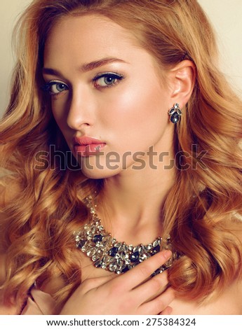 Fashion portrait of sexy blond girl with curly hair wearing beautiful jewelry and posing at studio
