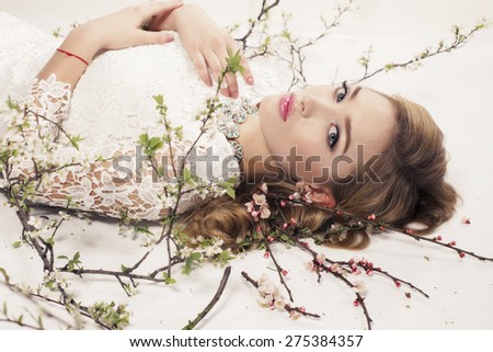 Fashion photo of sexy girl with curly hair wearing a lace dress,beautiful earrings and necklace,posing at studio around flowering trees
