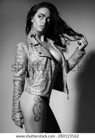 Fashion photo of sultry beautiful woman with brunette curls, tanned glowing skin and slim sexy body wearing  jacket in sequins and posing at studio