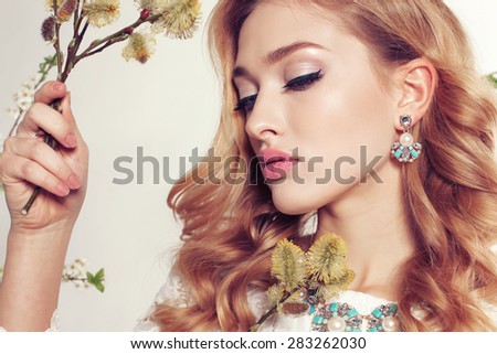 Fashion photo of sexy girl with curly hair wearing a lace dress,beautiful earrings and necklace,posing at sunny garden around flowering trees