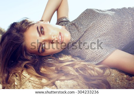 Fashion outdoor portrait of sexy beautiful elegant woman with long hair dressed in a luxurious evening dress posing on the summer beach