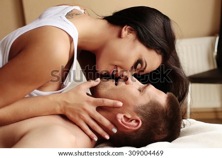 Fashion photo of two young beautiful lovers relax at the hotel on a bed,they are smiling,hugging and kissing