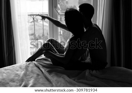Young couple resting in bed and looking out the window at the beautiful view of the city