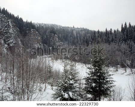 Snowy winter landscape: river, forest, rocks