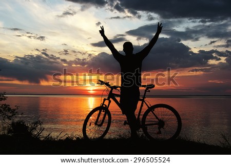 silhouette of a man with a mountain bike on the river bank at sunset
