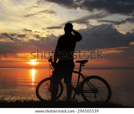 silhouette of a man with a mountain bike on the river bank at sunset