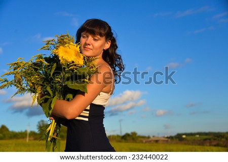 Young beautiful lady with a bouquet of sunflowers in field, blue sky on the background.