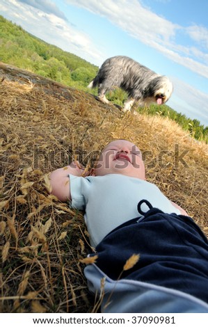 Dog guarding a baby laying on his back in the grass