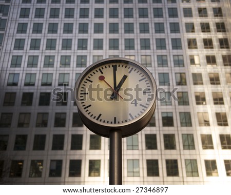Steel Clock Face with large steel and glass office building in background. Sunlight is reflecting on the glass windows