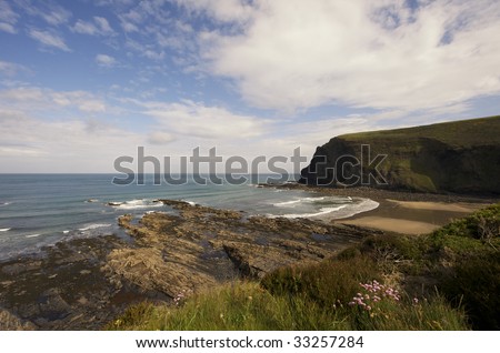 A sandy beach in Cornwall is surrounded by high cliffs. The early morning sunlight catches the white surf on the waves