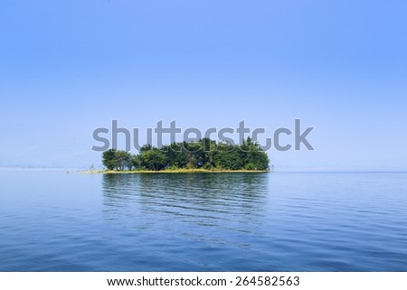 Small island covered with trees, The island is in the middle of the water and blue sky.