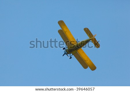 Yellow airplane (biplane) flying in a blue sky.