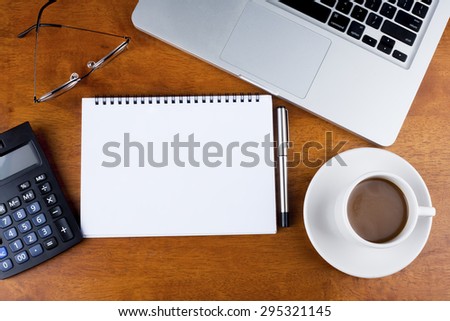 Empty notebook with a cup of coffee, calculator, spectacle and laptop on desk