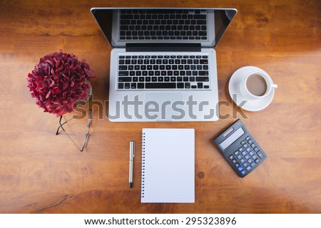 Working desk with spectacle, notebook, calculator, a cup of coffee, a flower jar and laptop
