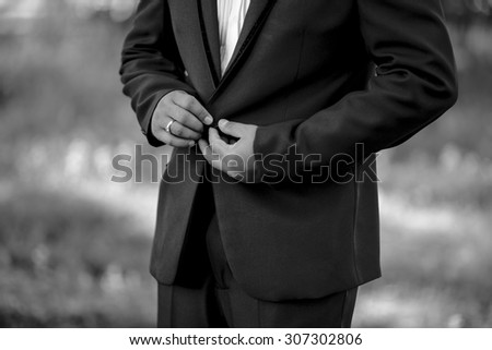 Closeup image of black and white half length body portrait of man wear a button on tuxedo on outdoor background location, wedding and business concept