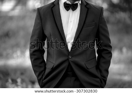 Closeup image of black and white half length body portrait of man wear a tuxedo with both hand in pocket on outdoor background location, wedding and business concept