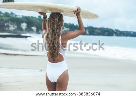 Beautiful girl on a surf board in the ocean. Girl with long hair in a white bathing suit in the ocean on the longboard. beautiful girl with a tattoo on his back in the ocean surf.