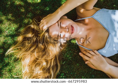 Beautiful girl with long white hair lies on green grass and smiles. Squint. A narrowed eye and a sly smile.