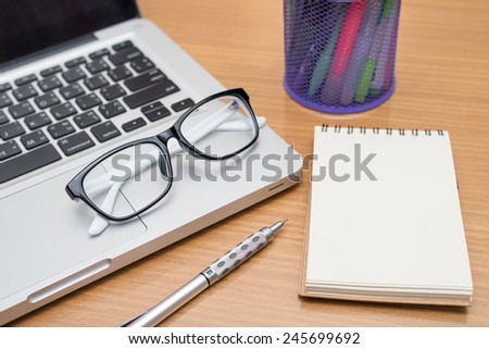 Blank business laptop, pen, note and glasses on wooden table