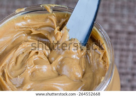 Macro close up of butter knife inserted into a freshly opened jar of creamy peanut butter.