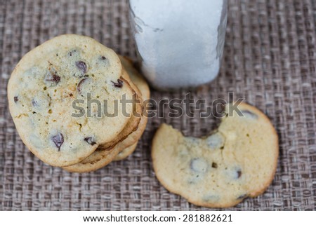 Chocolate chip cookies with milk.  Cookie has bite missing.