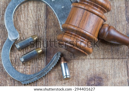Judge\'s wooden gavel laying on wood table with handcuffs that are in open position with bullets scattered around.