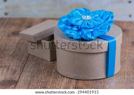 Rustic round brown gift box with blue ribbon and flower.