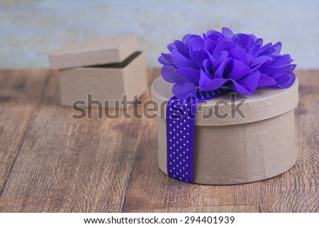 Rustic brown round gift box with a vivid purple flower and ribbon decorating it.