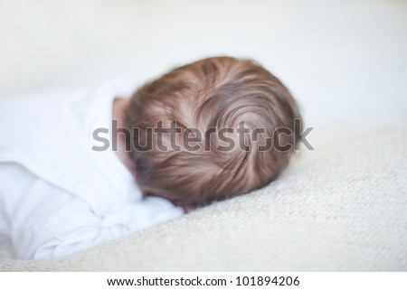 Portrait of a newborn baby lying on bed with back of head showing with a beautiful curl in the hair