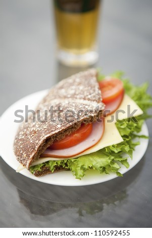 Close-up of a ham, cheese and tomato sandwich made with rye bread. Glass of green tea on the background