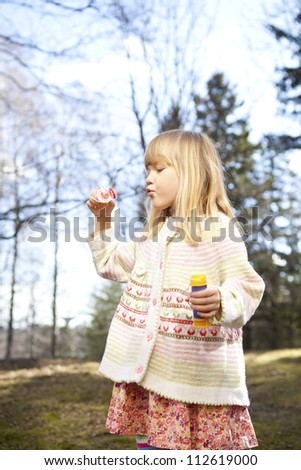 Little girl in cute clothes blowing bubbles outdoors